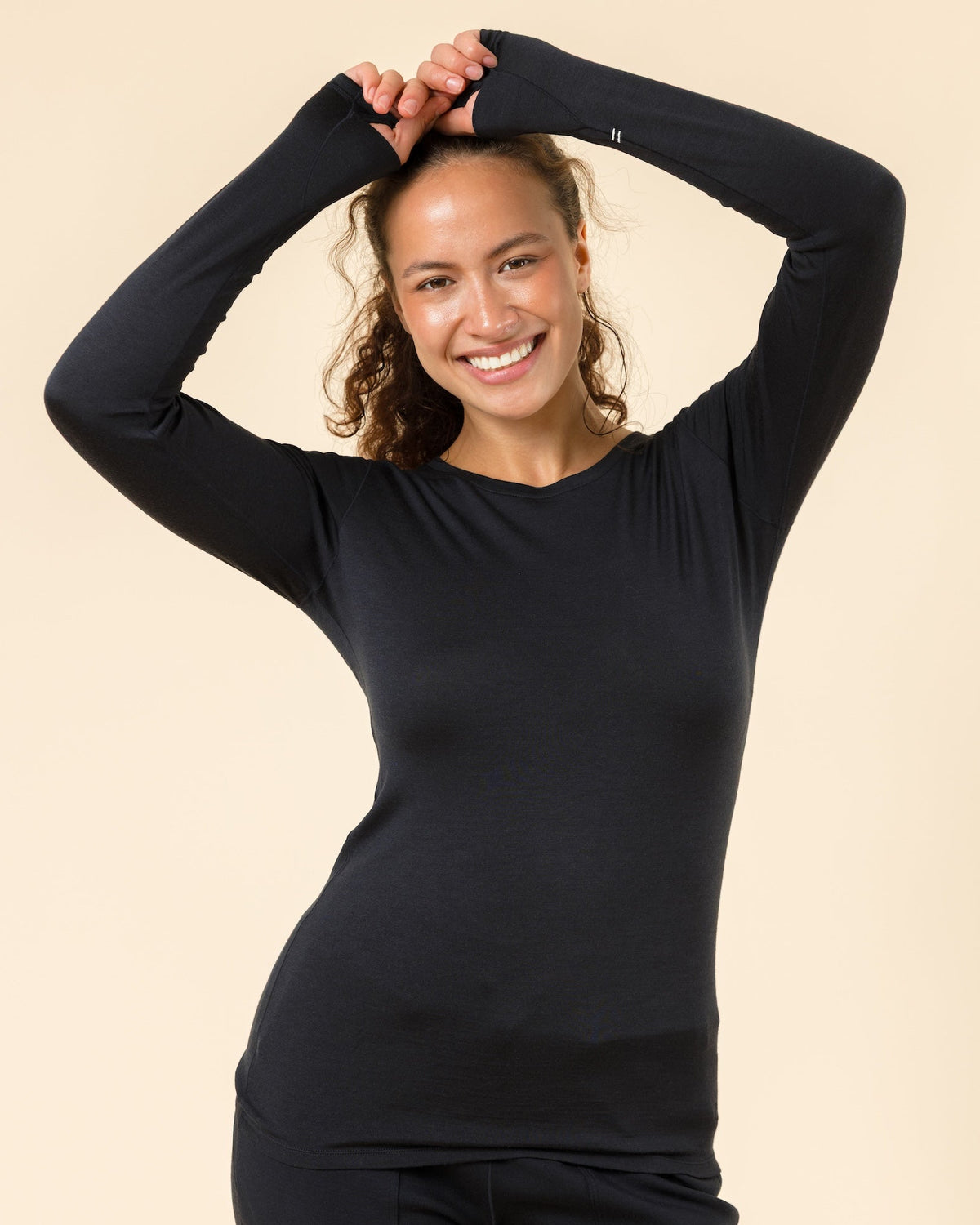 A woman modeling a black long-sleeve crewneck top and matching black leggings against a solid beige studio background.