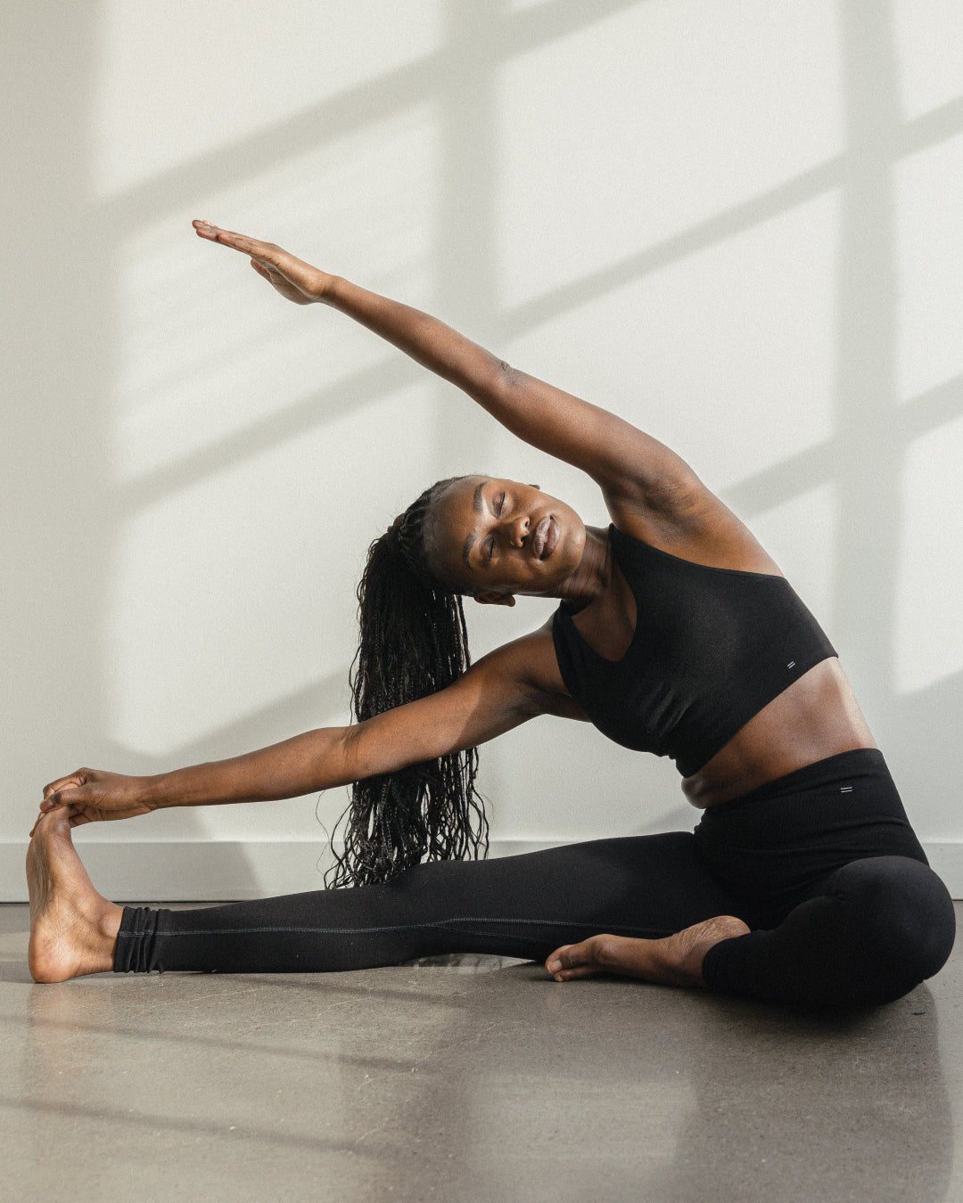 Woman stretching in black Merino Activewear. Wearing Merino compression leggings from BRANWYN, breathable Merino thermals.