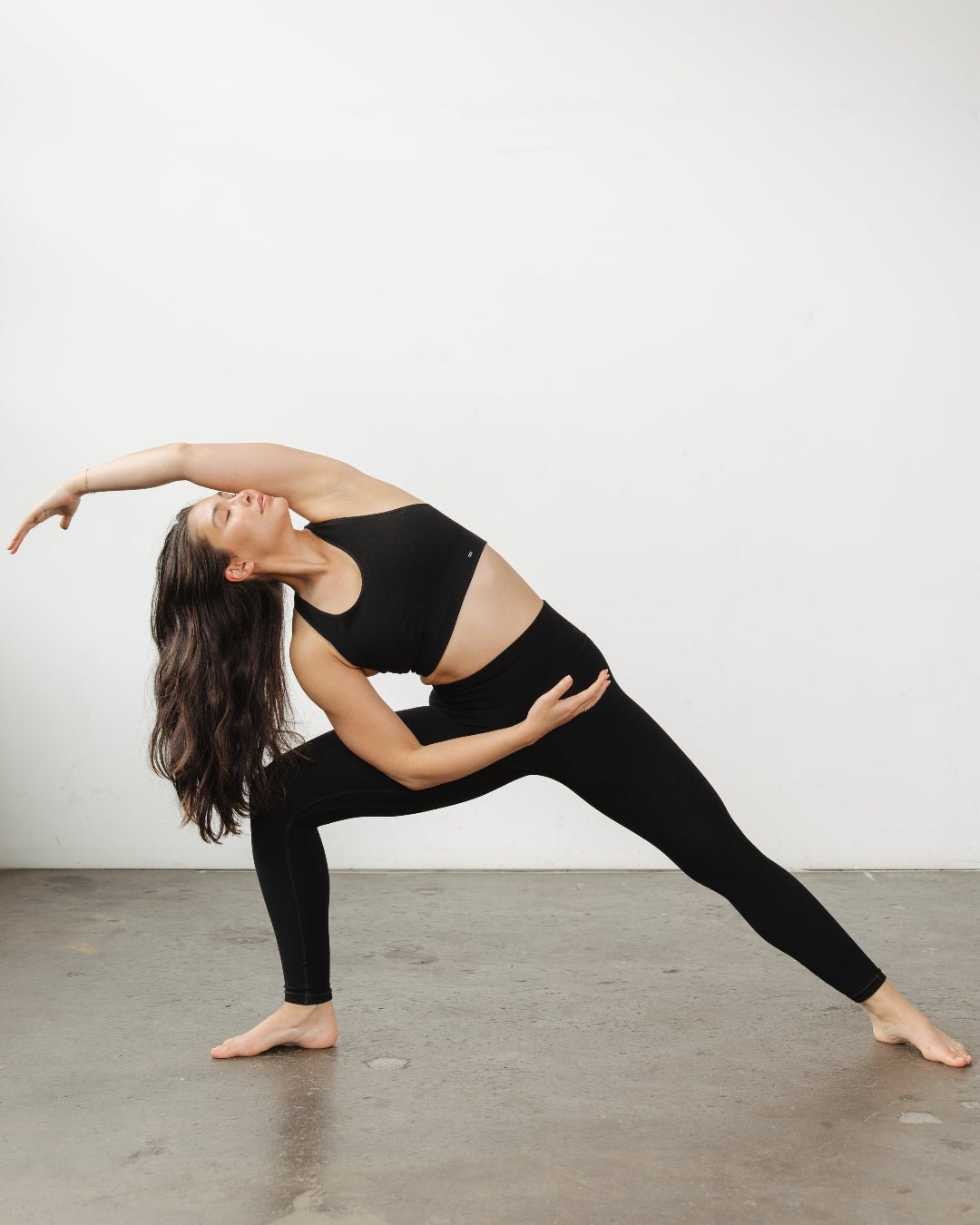 Woman stretching in a yoga pose wearing black Merino leggings and bra. Seamless Merino wool compression leggings made from sustainable natural fibers.