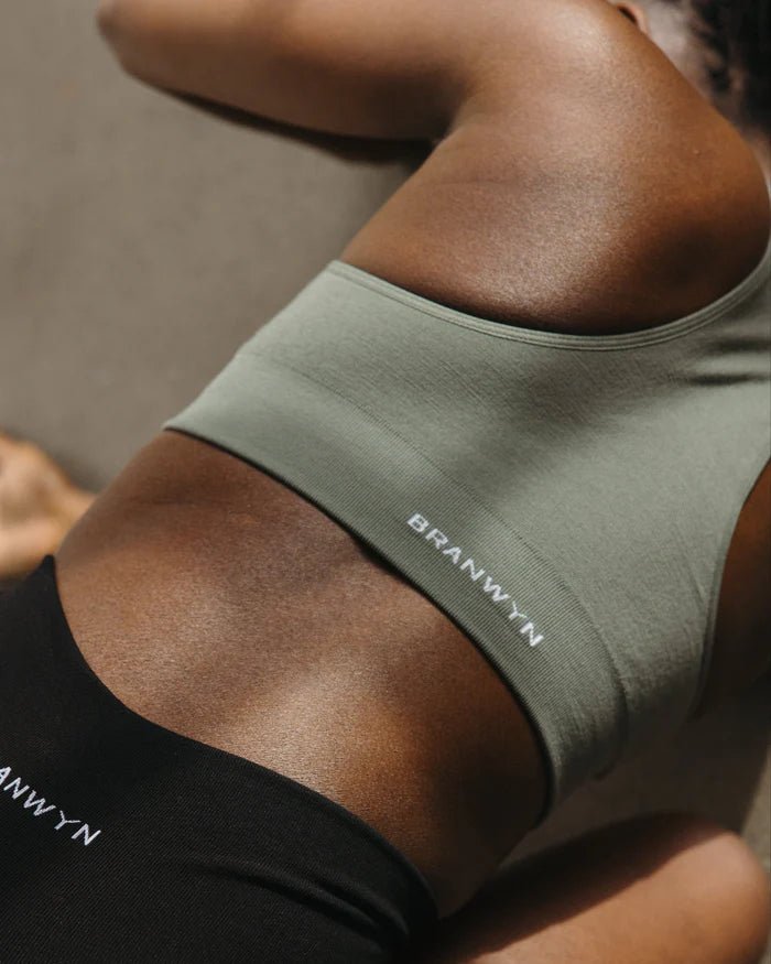Woman stretching in BRANWYN Racerback Sports Bra in agave green. Seamless Merino activewear built for performance and sustainability.