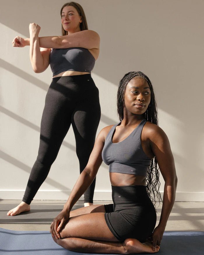 Two women stretching in yoga studio wearing grey Merino racerback sports bra by BRANWYN. Body hugging compressive Merino made for movement while remaining soft and breathable.