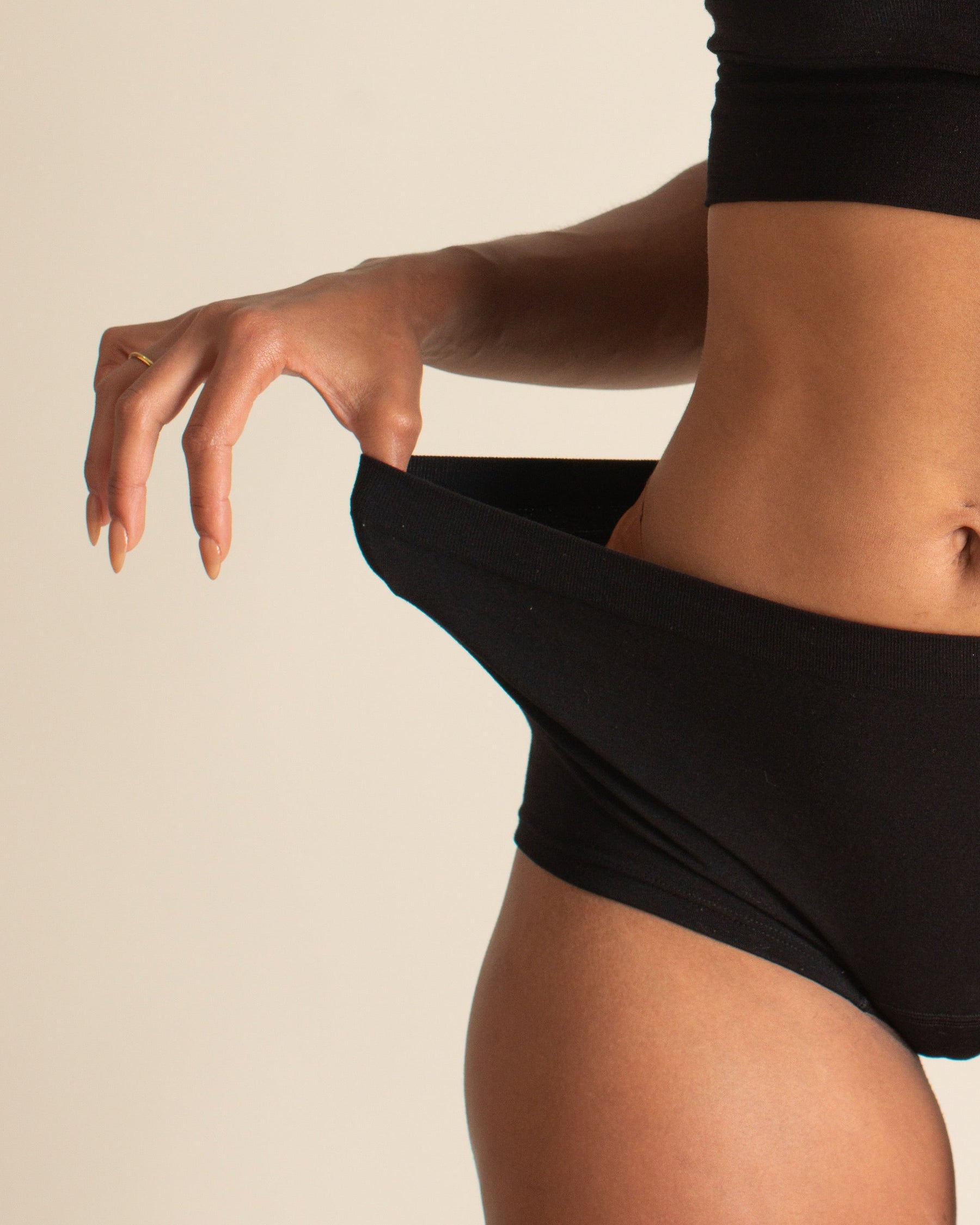 Woman demonstrating the stretch of the elastic free waistband on BRAWNYN women's seamless Merino wool Boyshorts underwear in Black. Great for skiing, travel underwear, and the best hiking underwear.