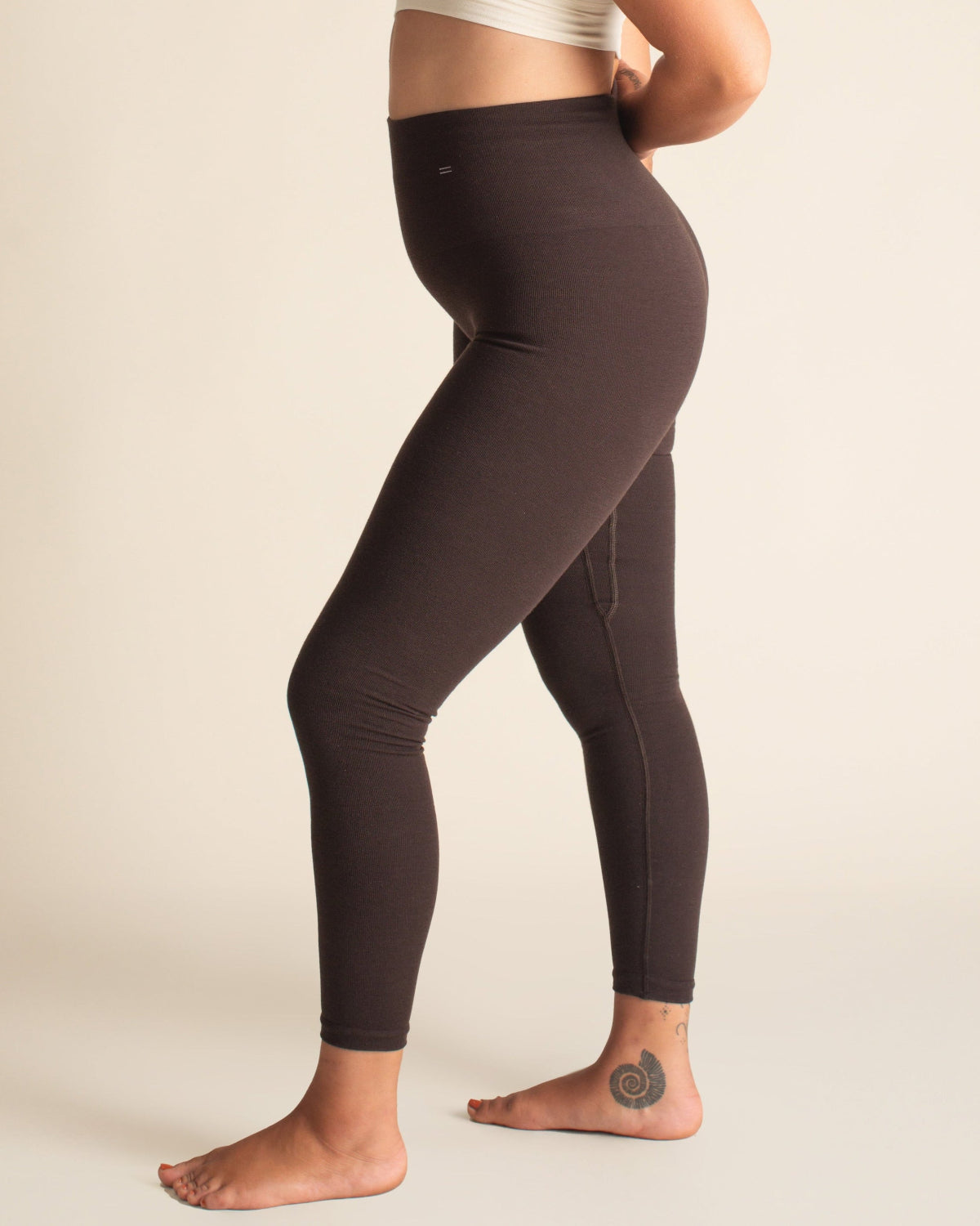 Woman wearing brown Merino wool leggings and a white sports bra on a beige background
