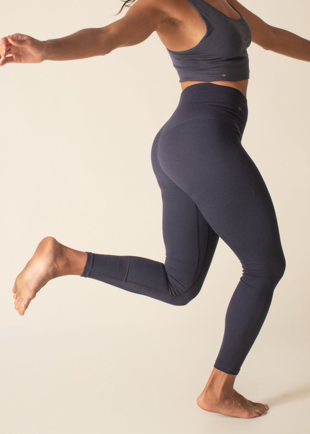 Woman in dark blue athletic wear posing against a beige background