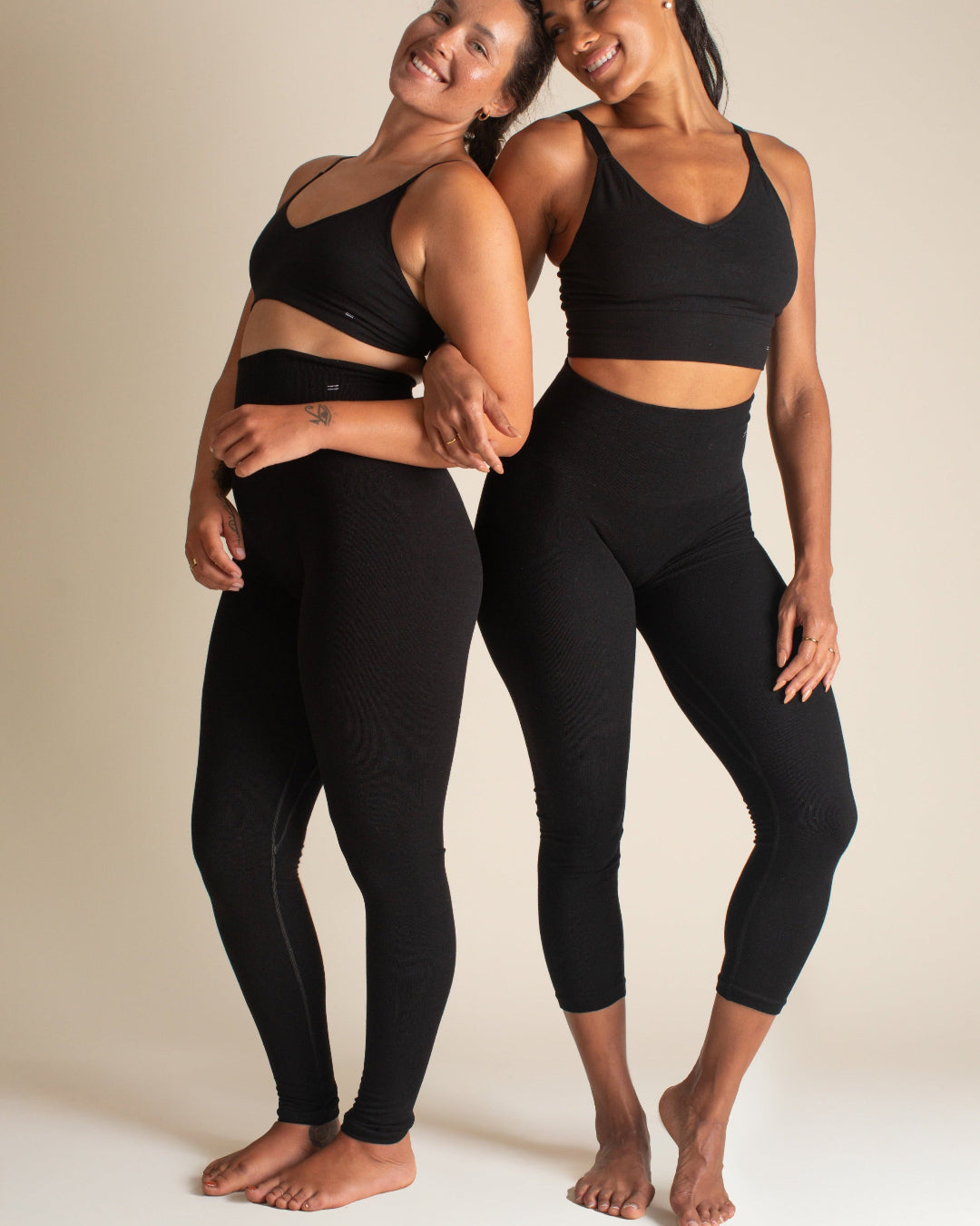 Two women holding arms wearing black, seamless Merino wool legging pants—perfect for yoga capris or a winter baselayer.