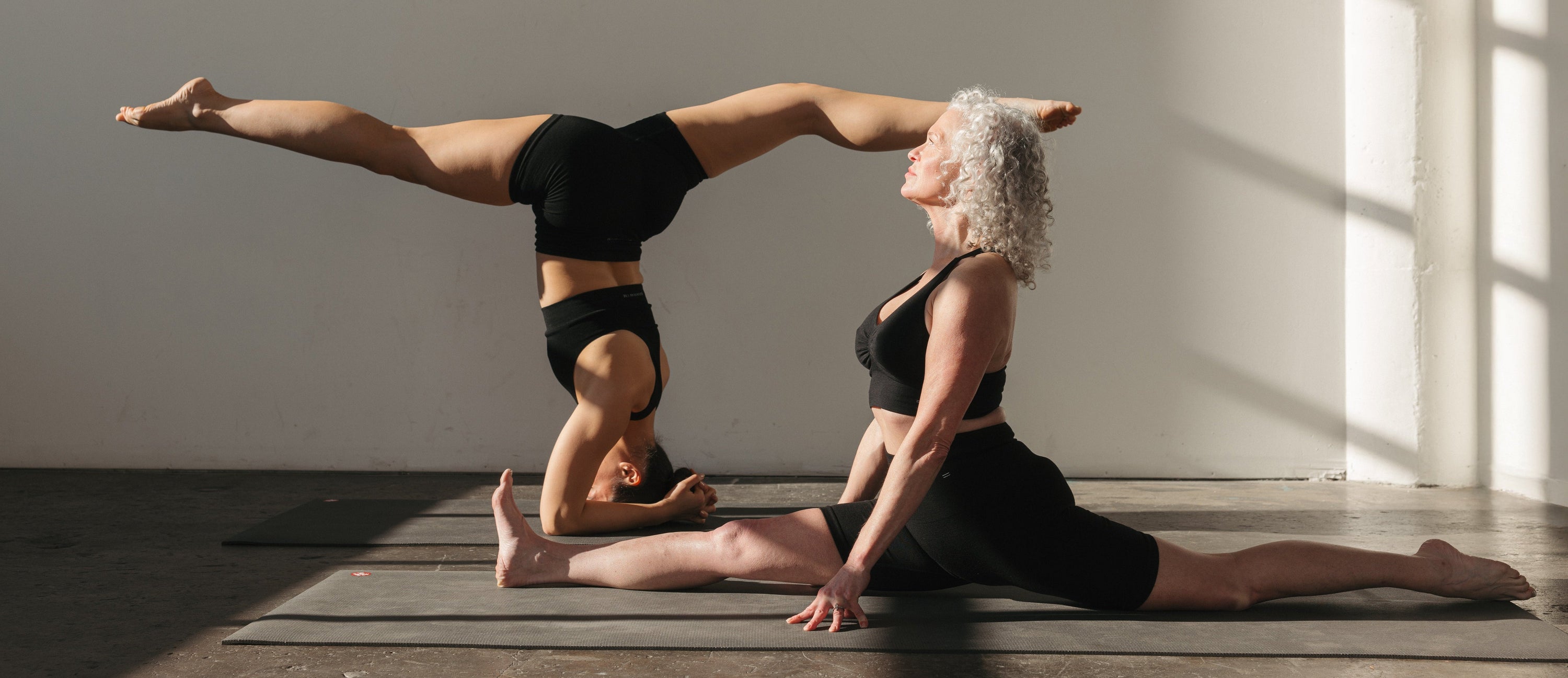 Two people performing a yoga pose in a well-lit room with wooden flooring.