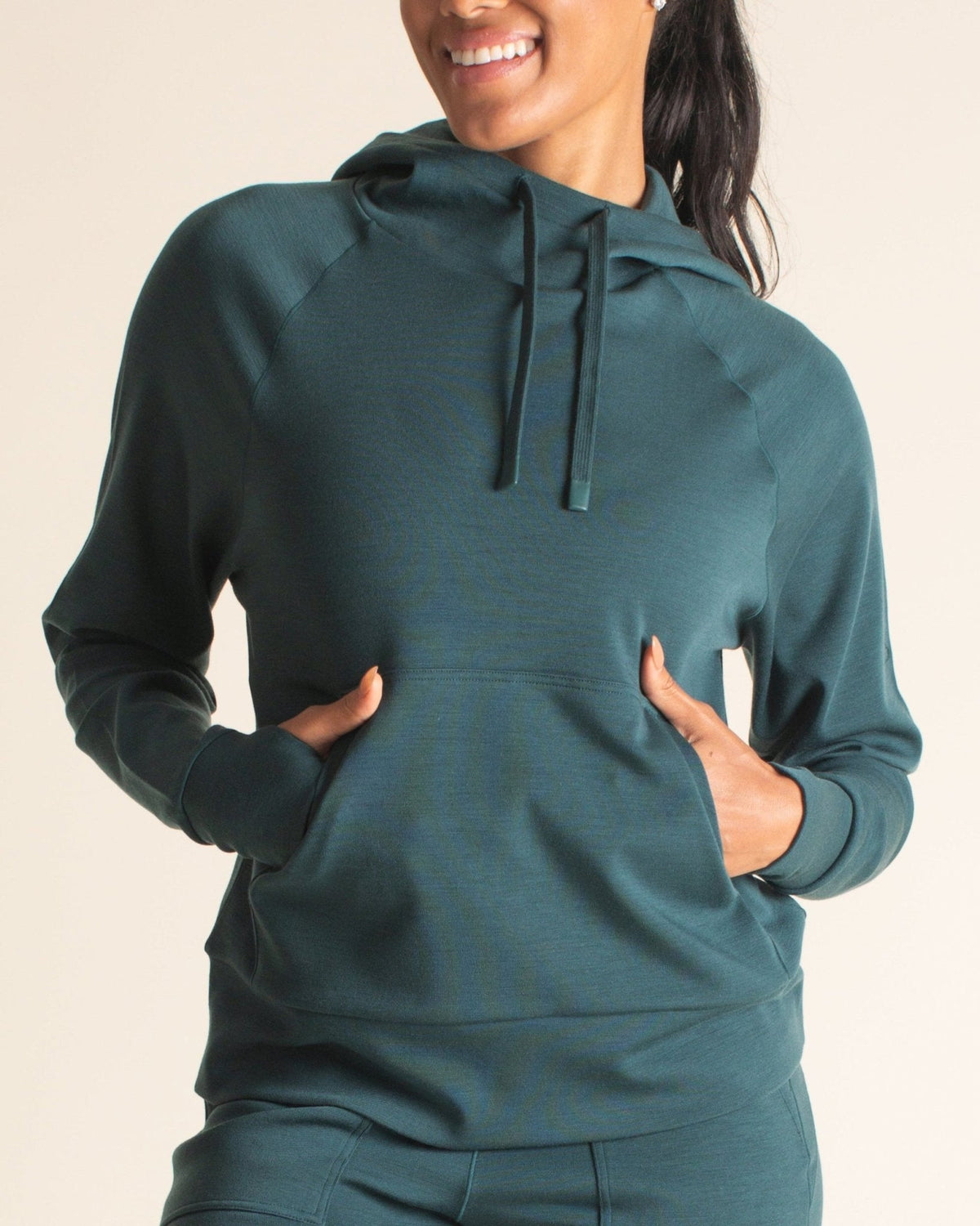 Woman smiling in BRANWYN Merino wool hoodie with front pockets. Lightweight, odor-resistant hoodie perfect for travel and layering on the go.