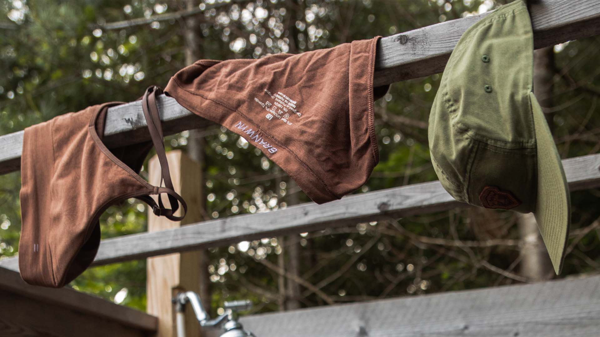 Merino wool hanging in outdoor shower to dry beside a green hat.