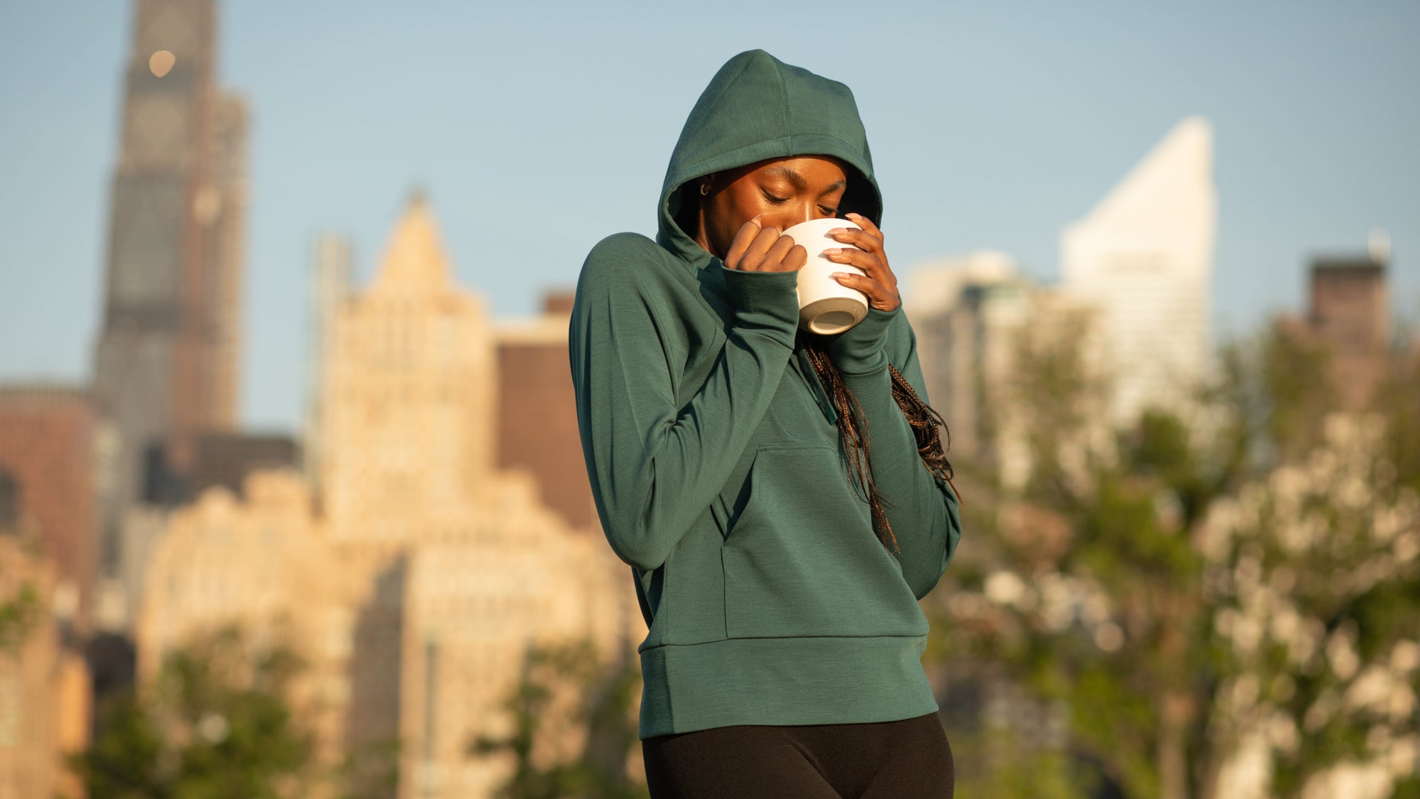 Woman sipping coffee in a BRANWYN Performance Innerwear Merino Hoodie in New York City
