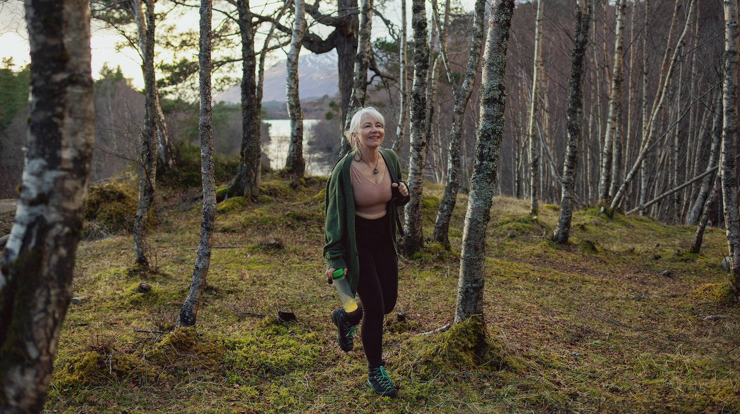 Woman hiking alone in the woods wearing Merino wool activewear and carrying a backpack and waterbottle.