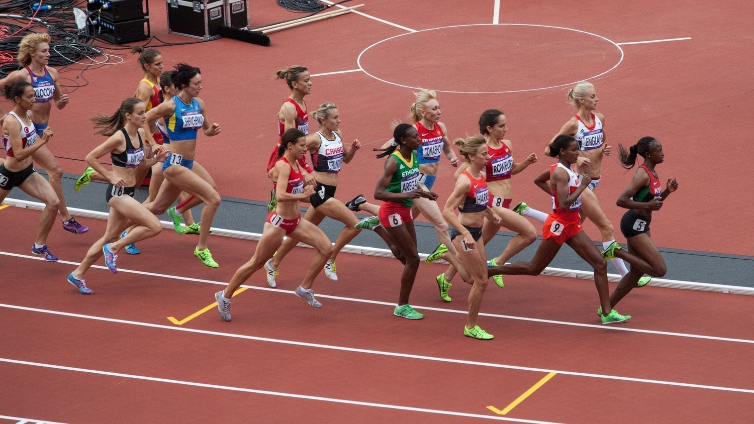 Olympic track runners racing in varied olympic uniforms.