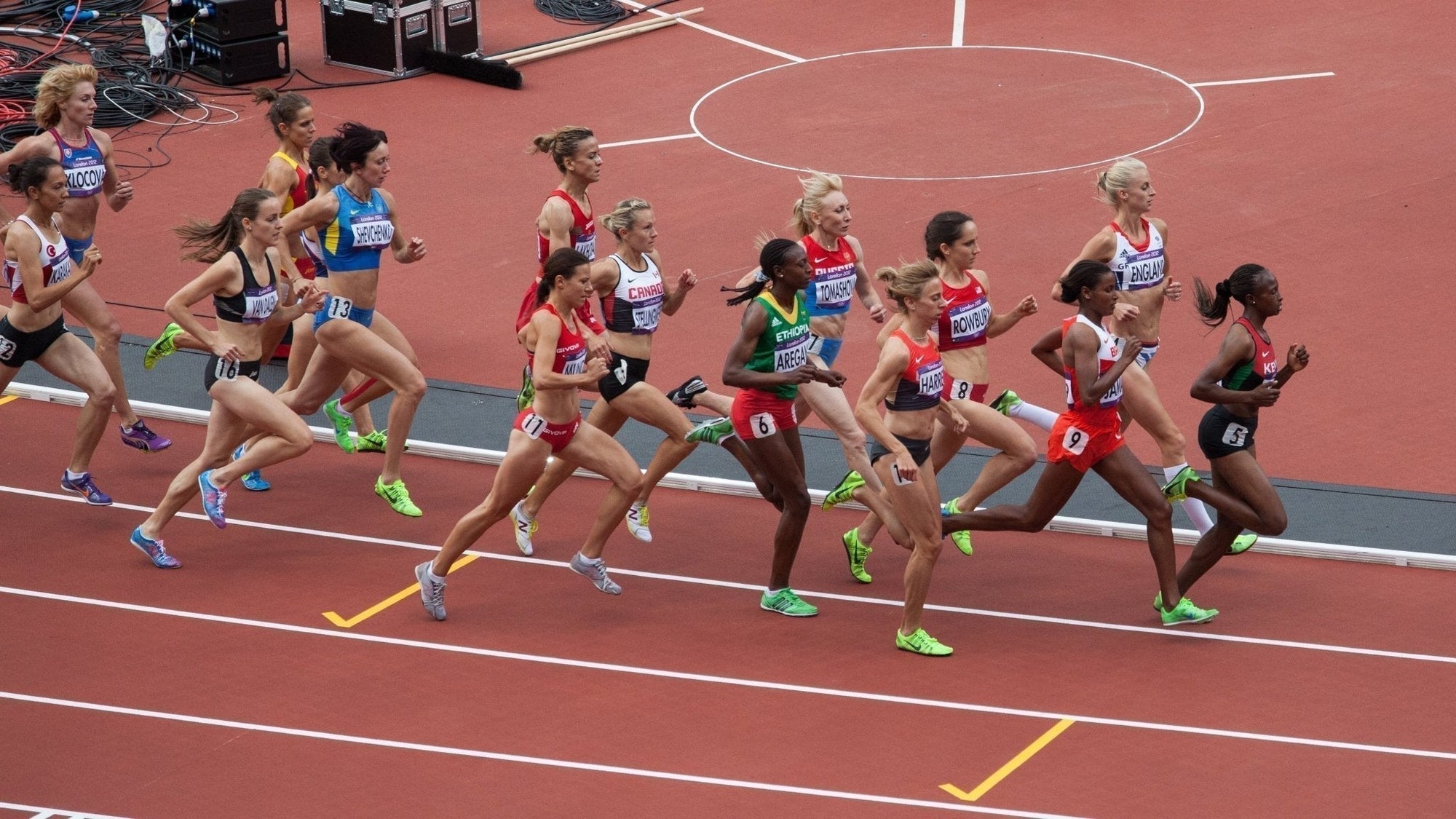 Olympic track runners racing in varied olympic uniforms.