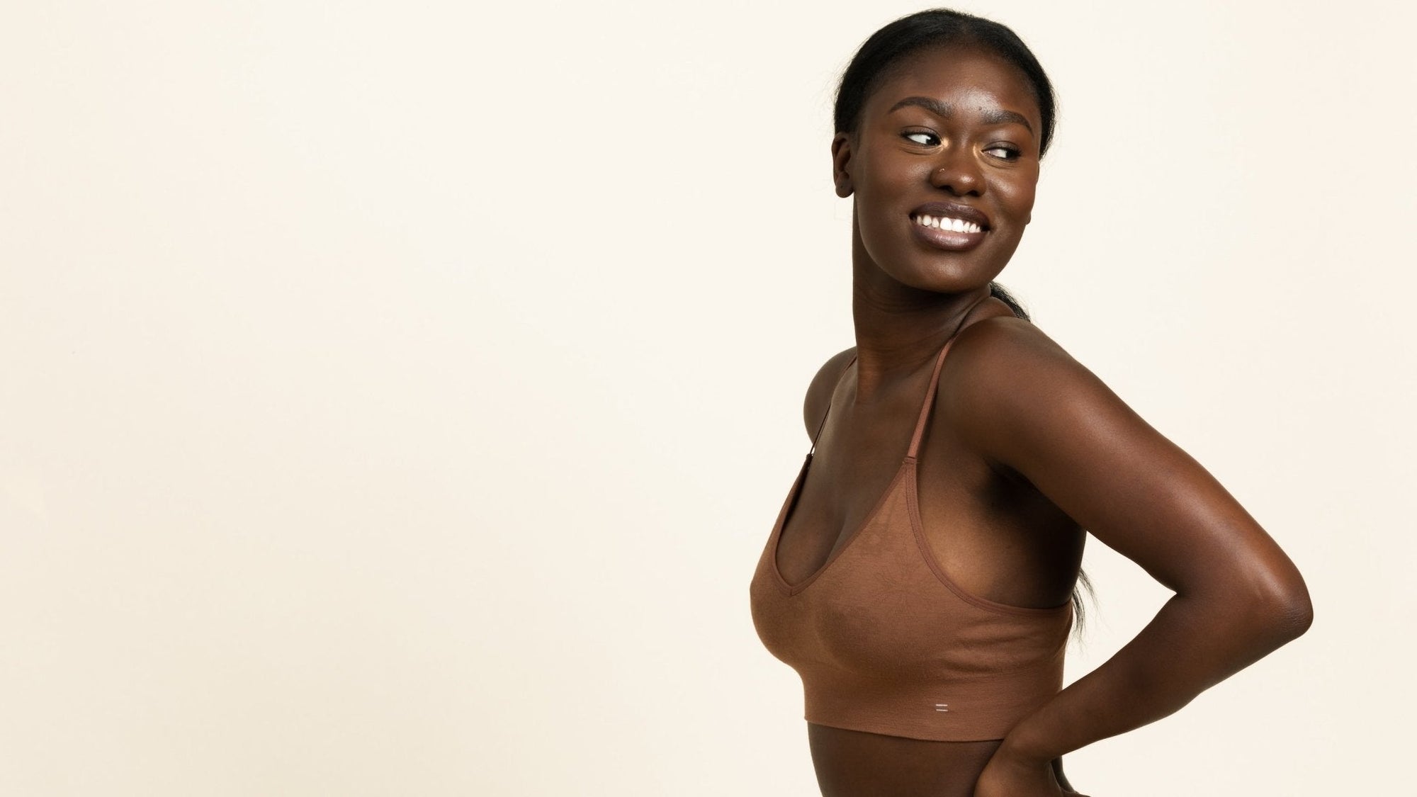 Woman similing , looking over her shoulder and wearing a brown seamless bra.