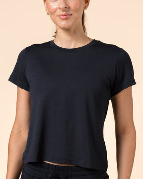 A woman modeling a black short-sleeve cropped t-shirt and matching black sweatpants against a solid beige studio background.
