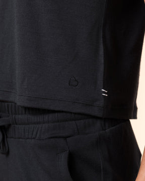 Close-up of a person wearing black lounge pants with a drawstring waistband and a black sleeveless top, against a plain warm beige background.