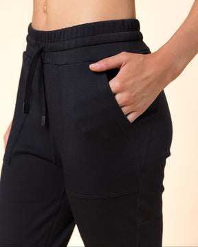 Close-up of a person wearing black wool joggers with side pockets, shown from the torso down against a plain beige studio background.