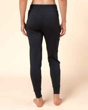 Rear view of a model wearing black Merino wool jogger pants against a solid beige studio background.
