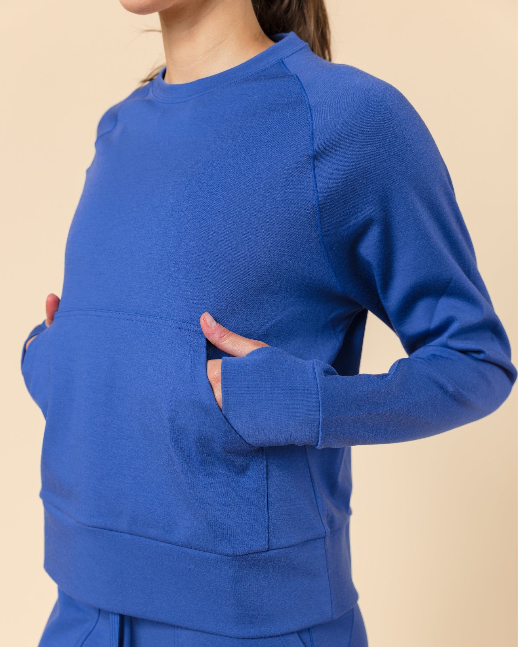 A woman wearing a matching royal blue sweatshirt and jogger pants set, shown from the neck down against a solid beige background.