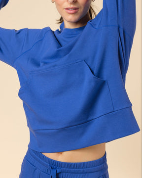 A woman modeling a bright royal blue cropped sweatshirt and matching sweatpants against a solid beige studio background.