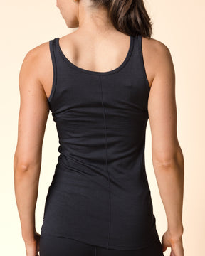 A woman shown from the back wearing a black athletic tank top and black leggings against a solid beige studio background.