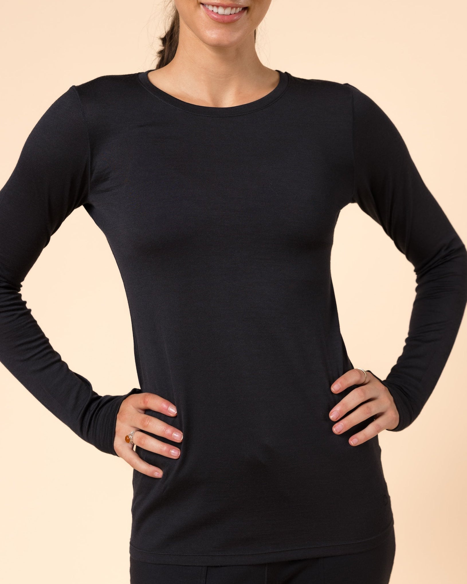 A woman modeling a black merino wool baselayer top against a solid beige studio background.