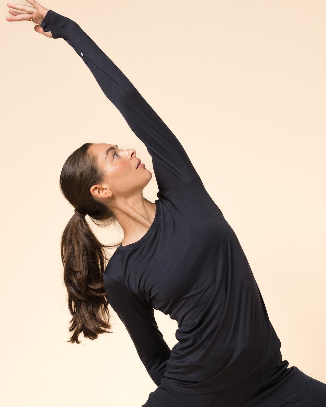 A woman in a black long-sleeve activewear set performs a yoga pose against a solid beige studio background.