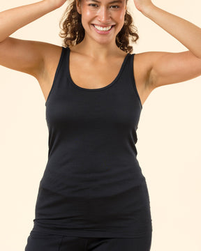 A woman smiling and posing in a black athletic tank top and matching black leggings against a solid light beige background.