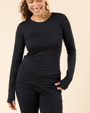 A woman smiling in a black long-sleeve crewneck merino wool baselayer against a solid beige studio background.