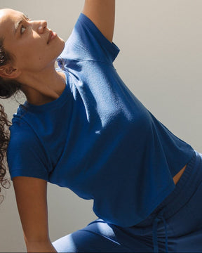 A woman in a blue activewear set performs a yoga pose on a mat in a bright studio with large windows casting shadows.