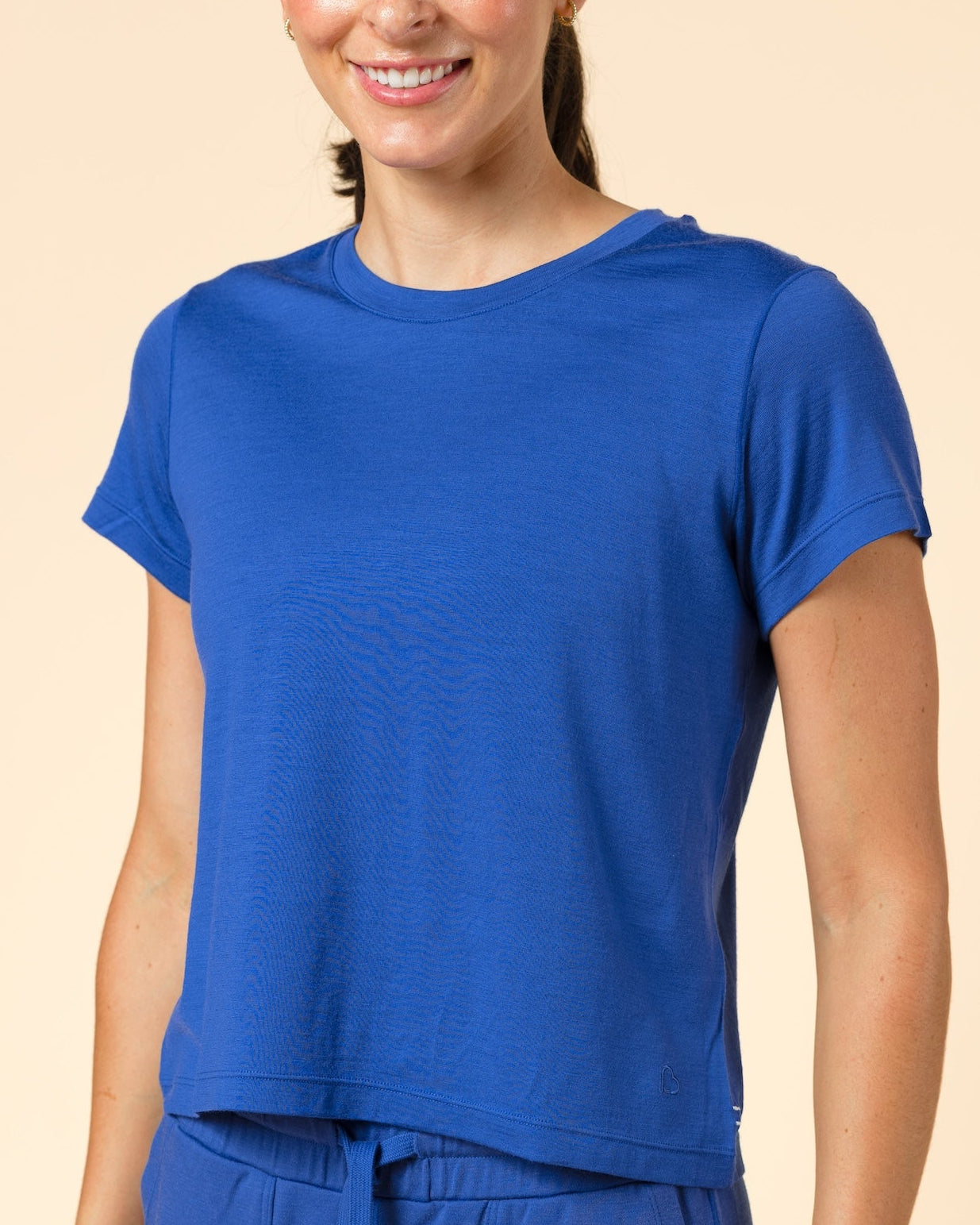 A woman modeling a matching royal blue short-sleeve crop top and jogger pants set against a solid beige studio background.