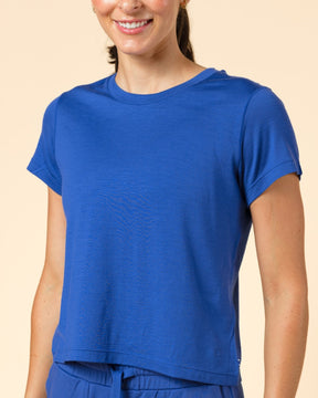 A woman modeling a matching royal blue short-sleeve crop top and jogger pants set against a solid beige studio background.