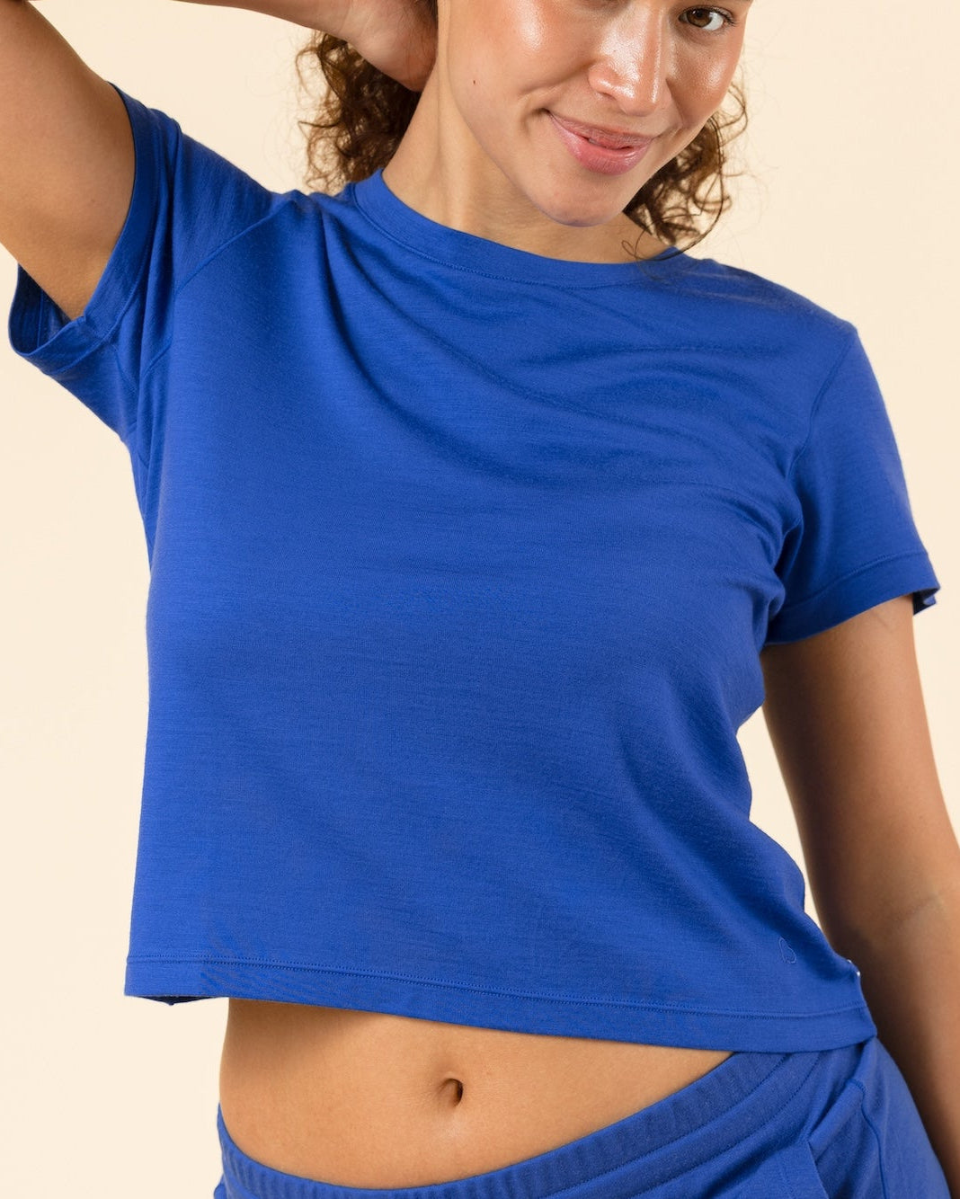 A woman modeling a matching royal blue two-piece lounge set consisting of a short-sleeve crop top and drawstring sweatpants, set against a solid beige background.