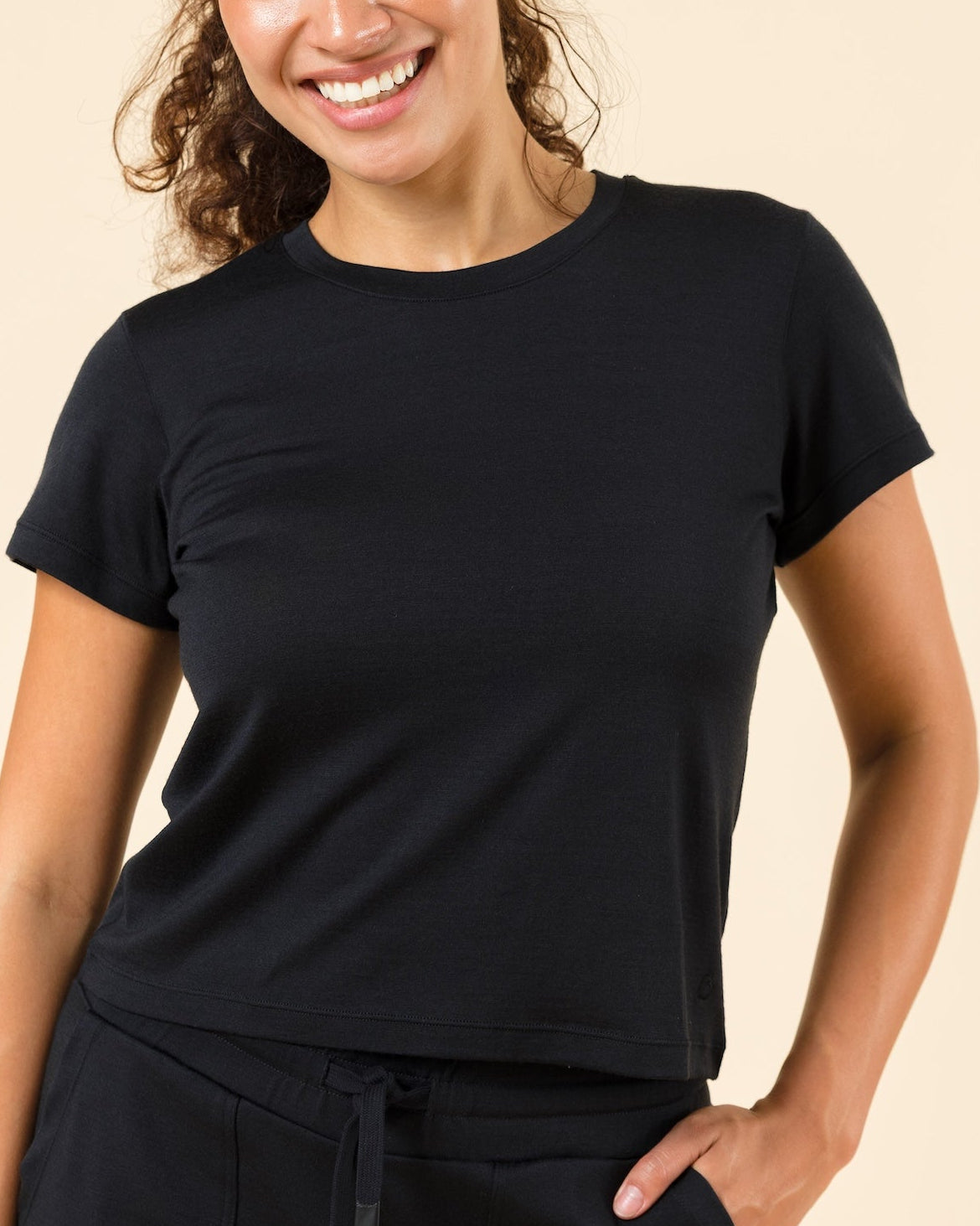 A woman modeling a black short-sleeve crewneck t-shirt and matching black drawstring sweatpants against a solid beige studio background.