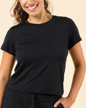 A woman modeling a black short-sleeve crewneck t-shirt and matching black drawstring sweatpants against a solid beige studio background.