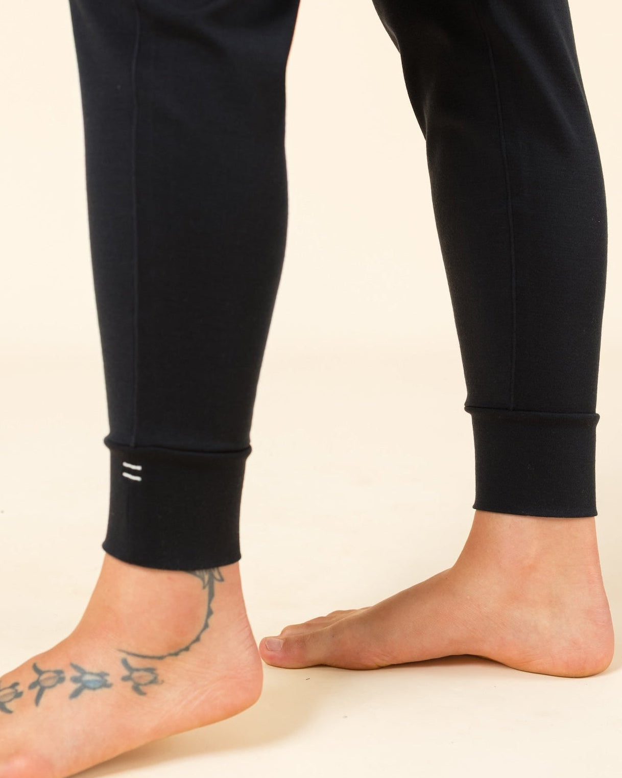 Close-up of Merino wool joggers ankle cuff details photographed against a plain warm cream studio background.
