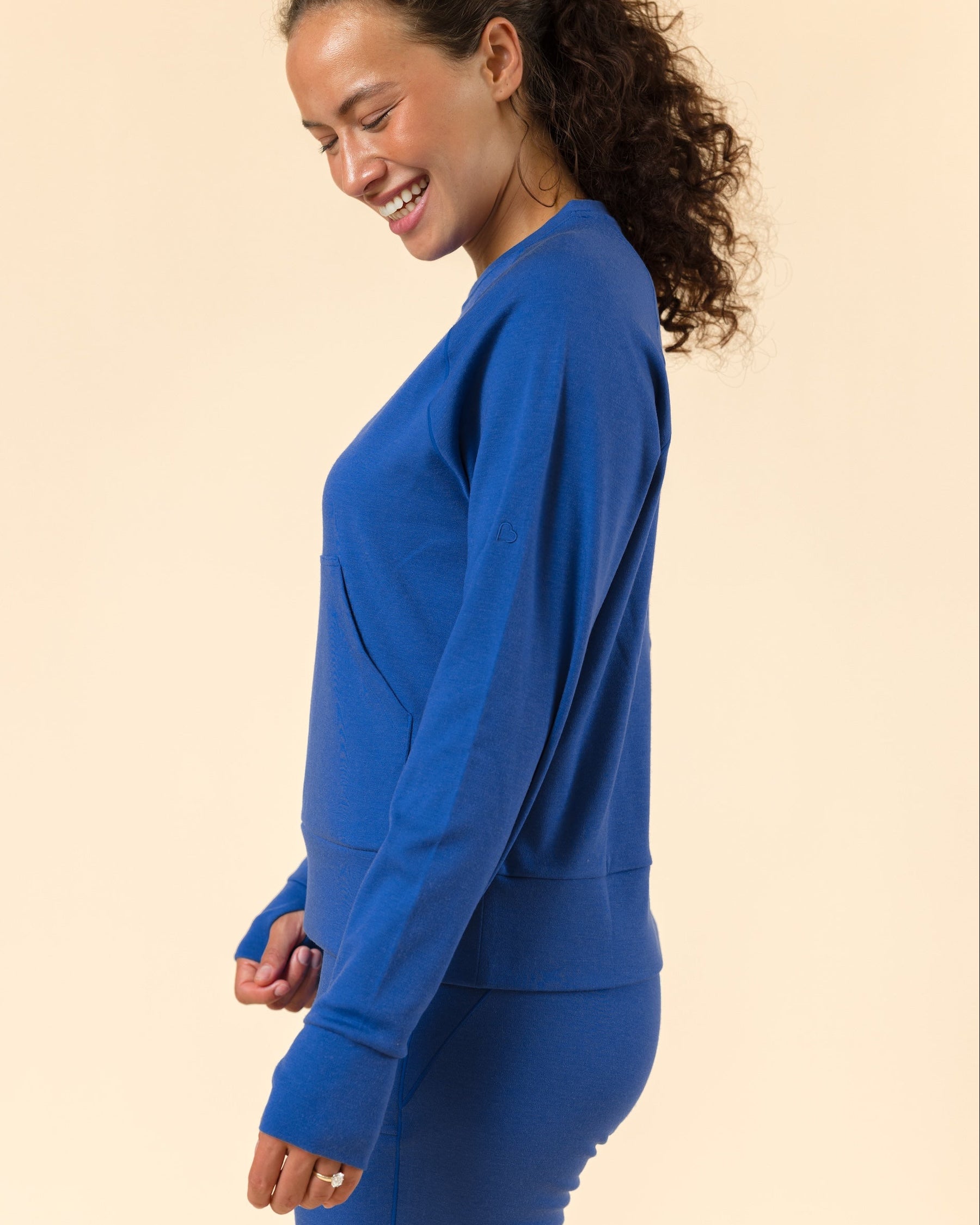 A woman wearing a matching royal blue sweatshirt and leggings set, shown in profile against a solid beige studio background.