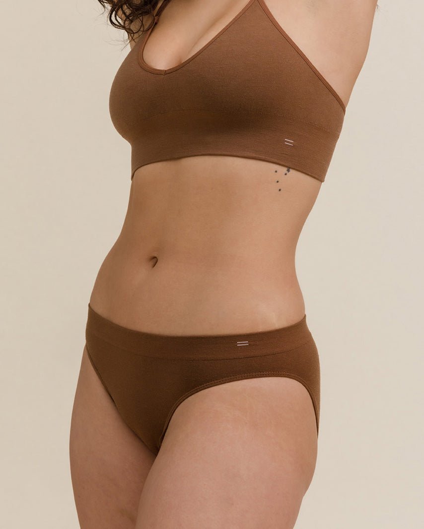 Woman wearing dark nude brown BRANWYN Essential Bikni underwear and matching bra, showing seamless design.
