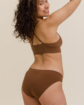 Back view of woman with curly hair smiling in BRANWYN seamless Merino wool bra and underwear set in dark nude brown