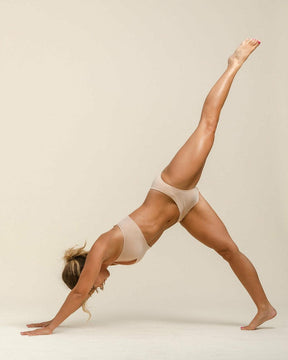 Woman in three legged dog yoga pose in matching light nude BRANWYN Merino Wool underwear set.