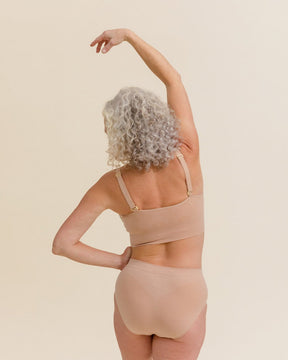 Model stretching in the comfiest Merino underwear set in light nude wearing BRANWYN's Essential Hipster high waisted seamless panties.