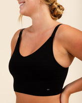 Model smiling while showing side angle of a black natural fiber bra, Merino bra for large breasts.