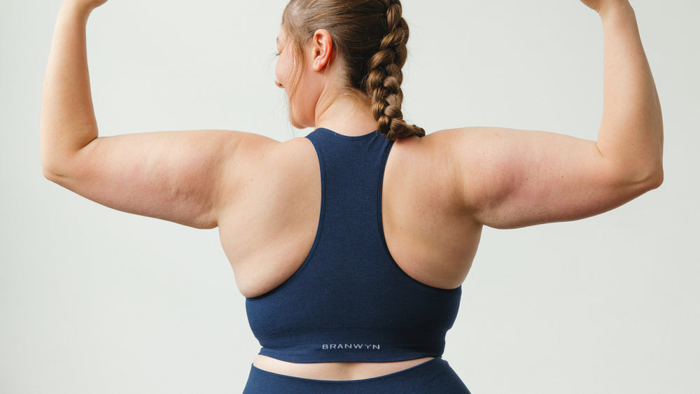 Person wearing a blue sports bra and leggings flexing their muscles on a plain background