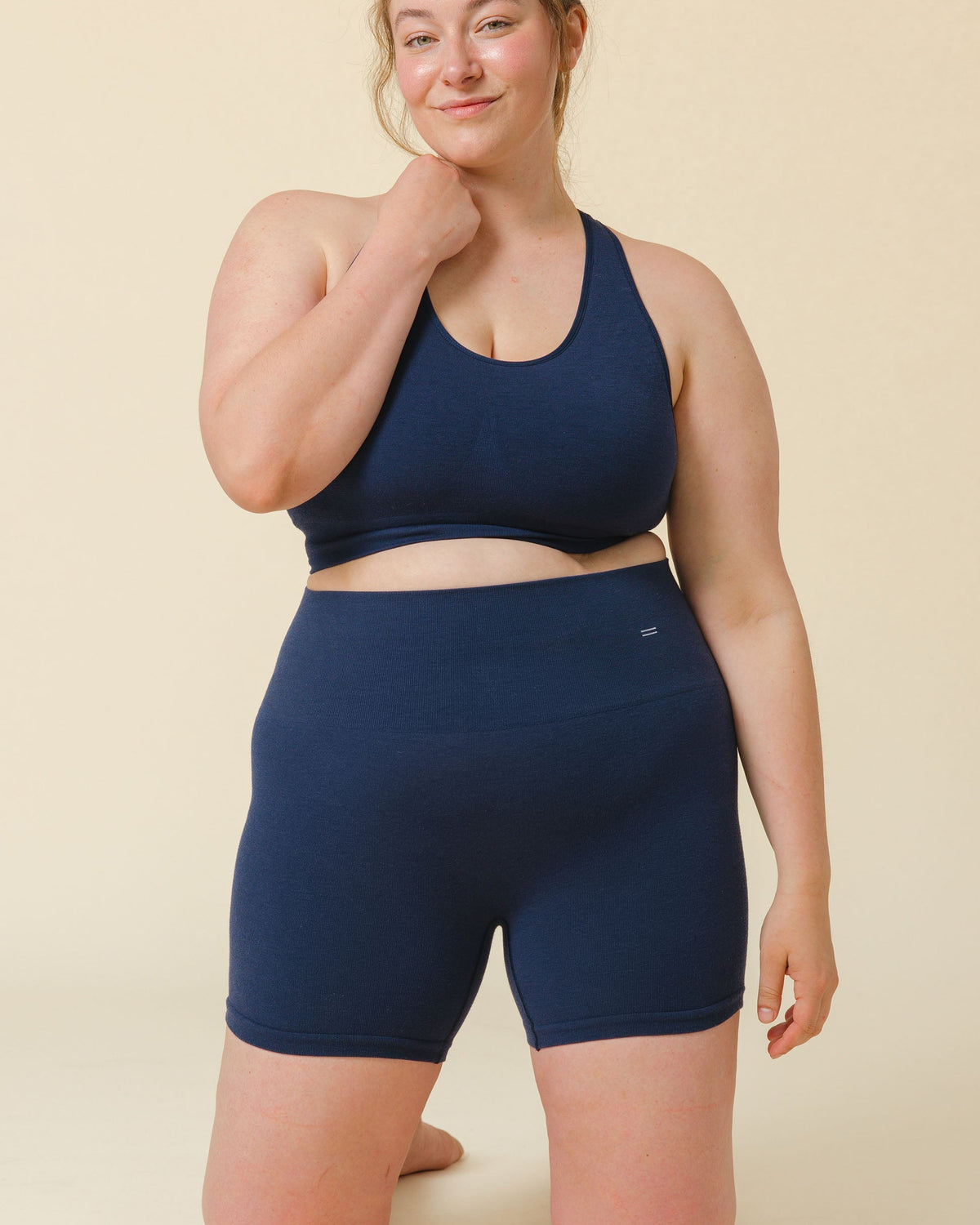Woman wearing a navy blue sports bra and shorts set on a beige background