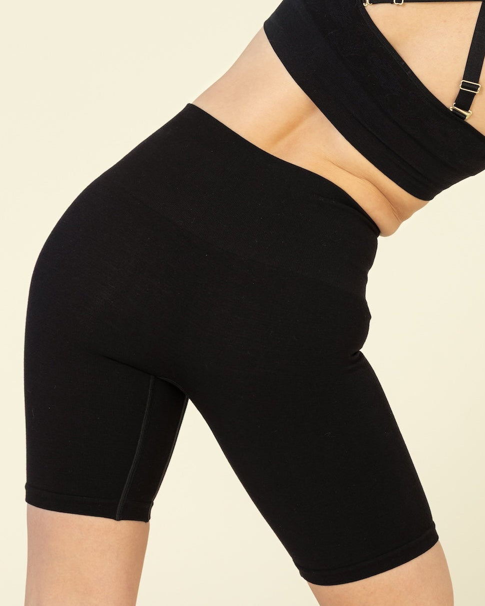 Person wearing a black sports bra and shorts on a beige background