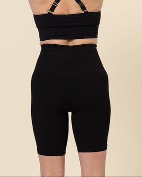 Person wearing a black sports bra and high-waisted black shorts on a beige background