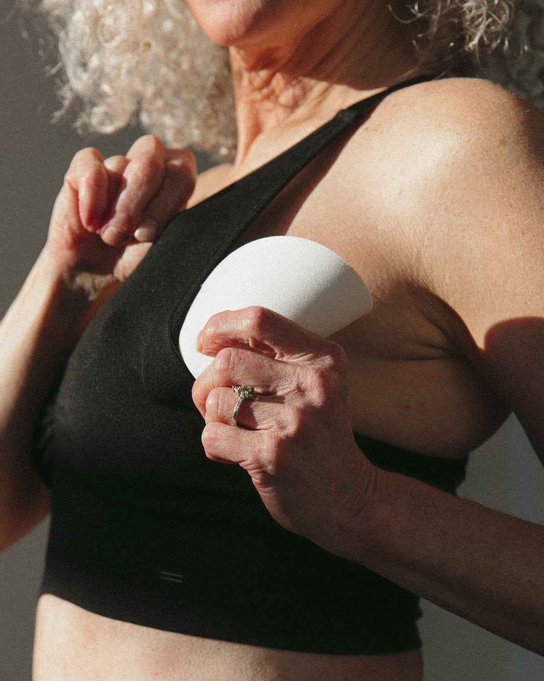 A woman wearing a black sports bra pulls out a removable bra pad.