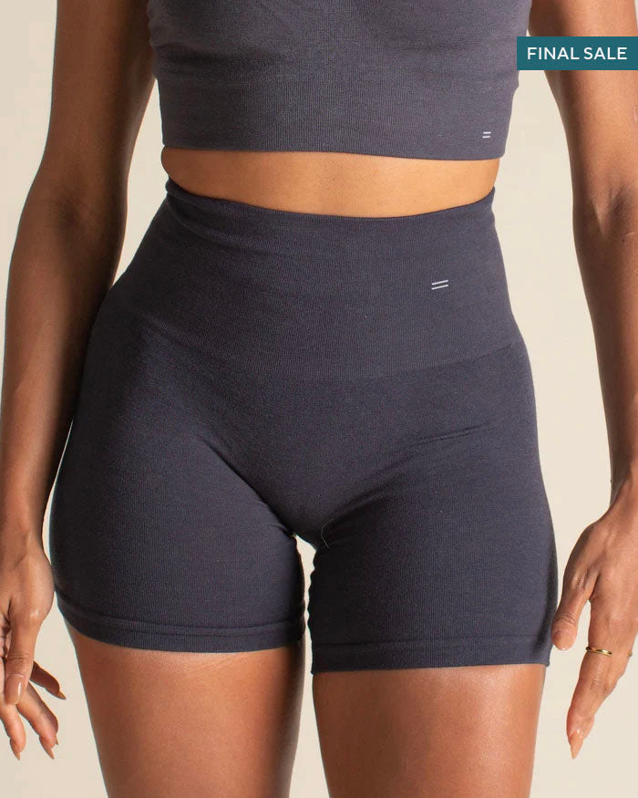 Woman wearing a dark gray sports bra and shorts on a beige background