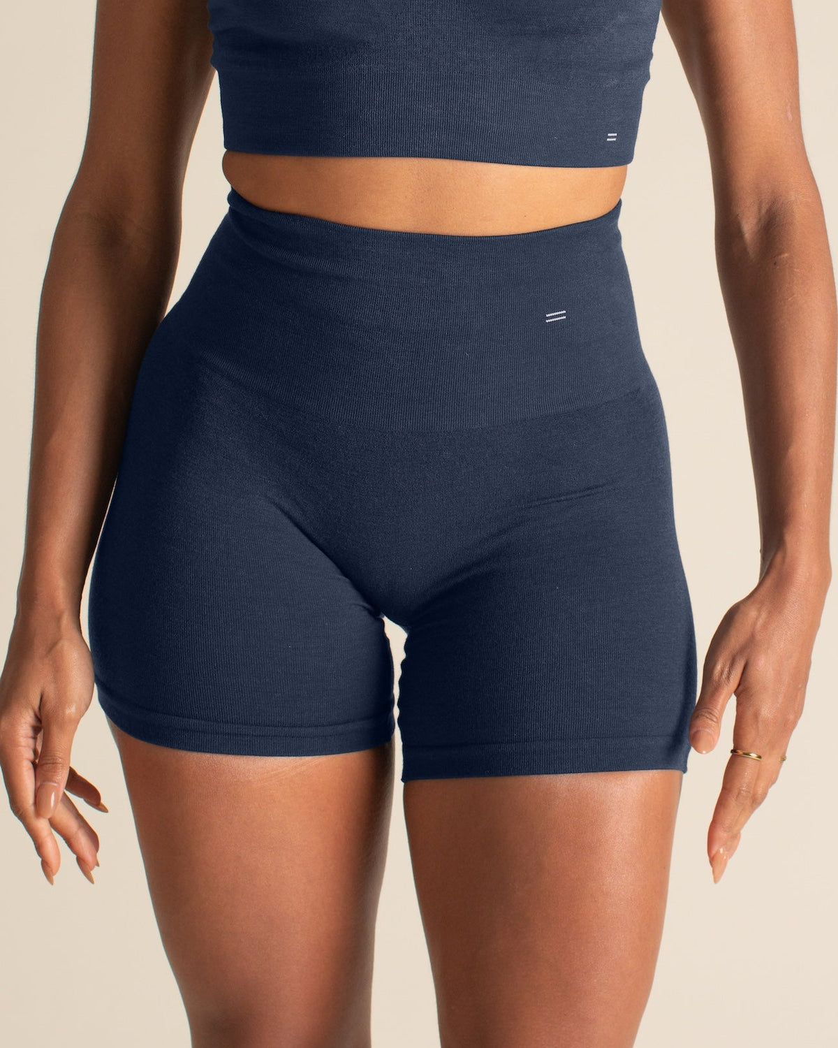 Woman wearing a navy blue sports bra and shorts set on a beige background