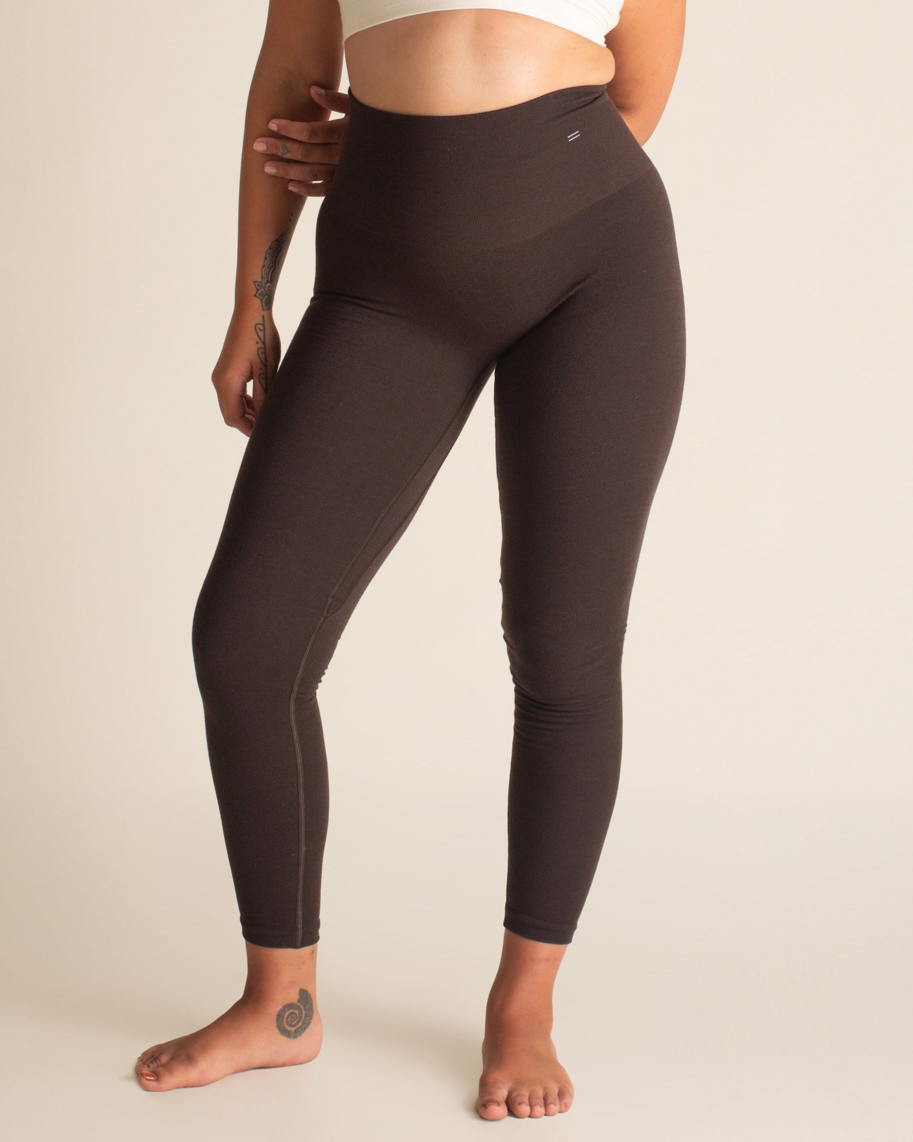 Woman wearing a white sports bra and brown leggings on a beige background