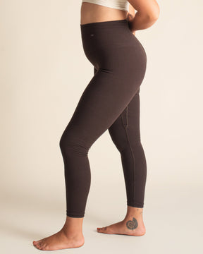 Woman wearing brown leggings and a white sports bra on a beige background